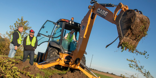 An instructor watching a student operate a backhoe