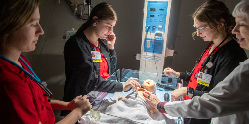 nursing students treat a sim baby while instructor watches