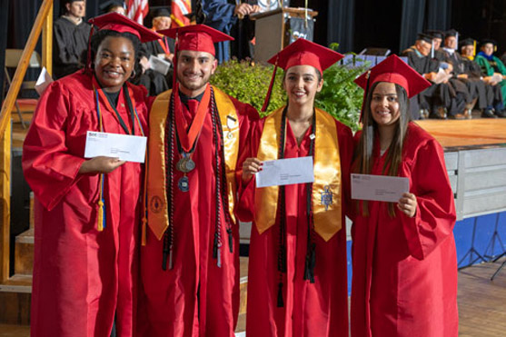 Students in red graduation caps and gowns smiling and holding envelopes